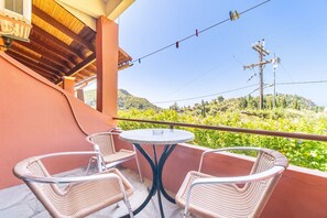 A balcony with wicker chairs and a small round table, overlooking a lush green hillside.
