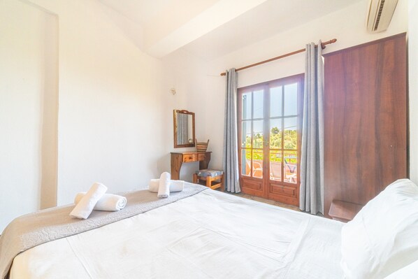 A hotel room with a bed, a desk, a chair, a window with curtains, and a view of the outdoors.