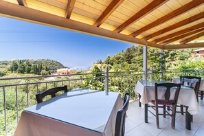 An outdoor terrace with tables and chairs, a wooden pergola, and a view of a hillside.