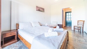 Un dormitori amb un llit, taules de nit, una cadira i una porta que condueix a una altra habitació.