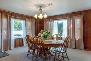 Un comedor con una mesa y sillas de madera, una araña y una ventana con cortinas.