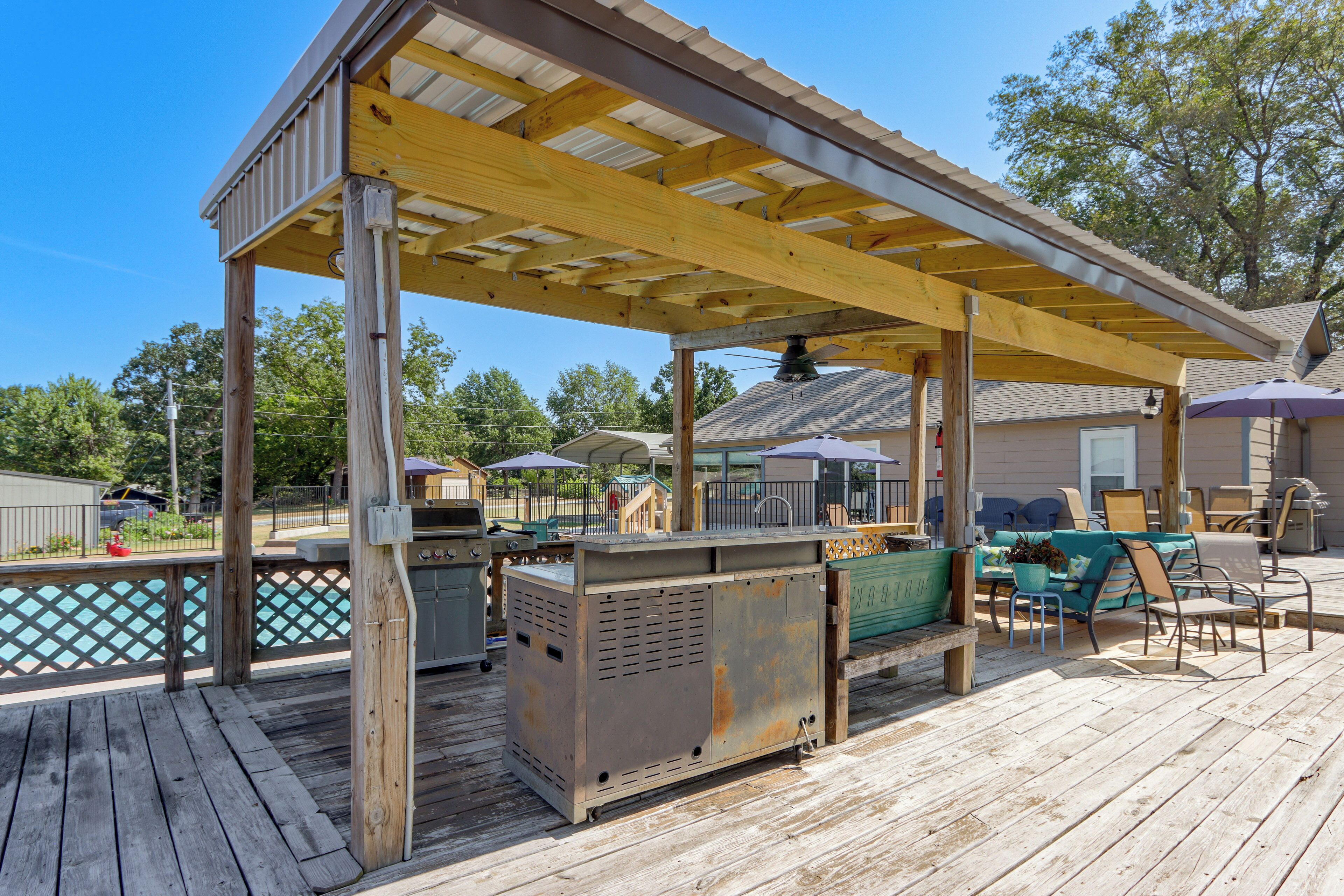 A covered outdoor deck with a grill, seating area, and poolside view.