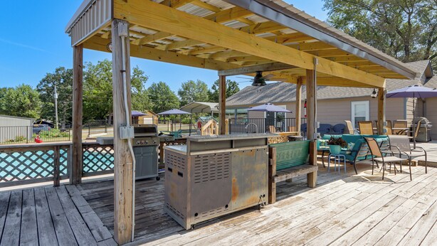 A covered outdoor deck with a grill, seating area, and poolside view.