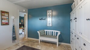 A hallway with a blue wall, a white bench, a welcome sign, and a door leading to another room.