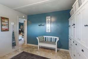 A hallway with a blue wall, a white bench, a welcome sign, and a door leading to another room.