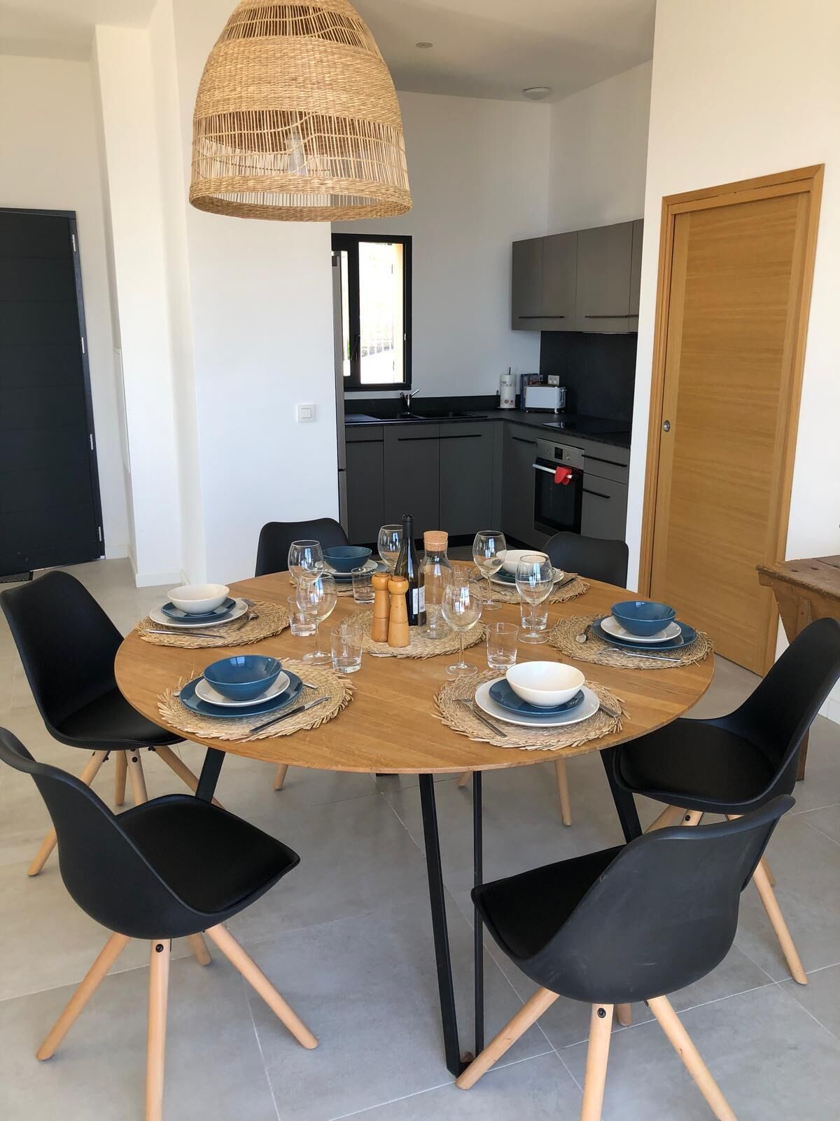 A dining area with a round table set for four, black chairs, and a woven pendant light.