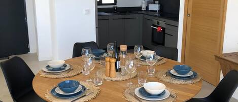 A dining area with a round table set for four, black chairs, and a woven pendant light.