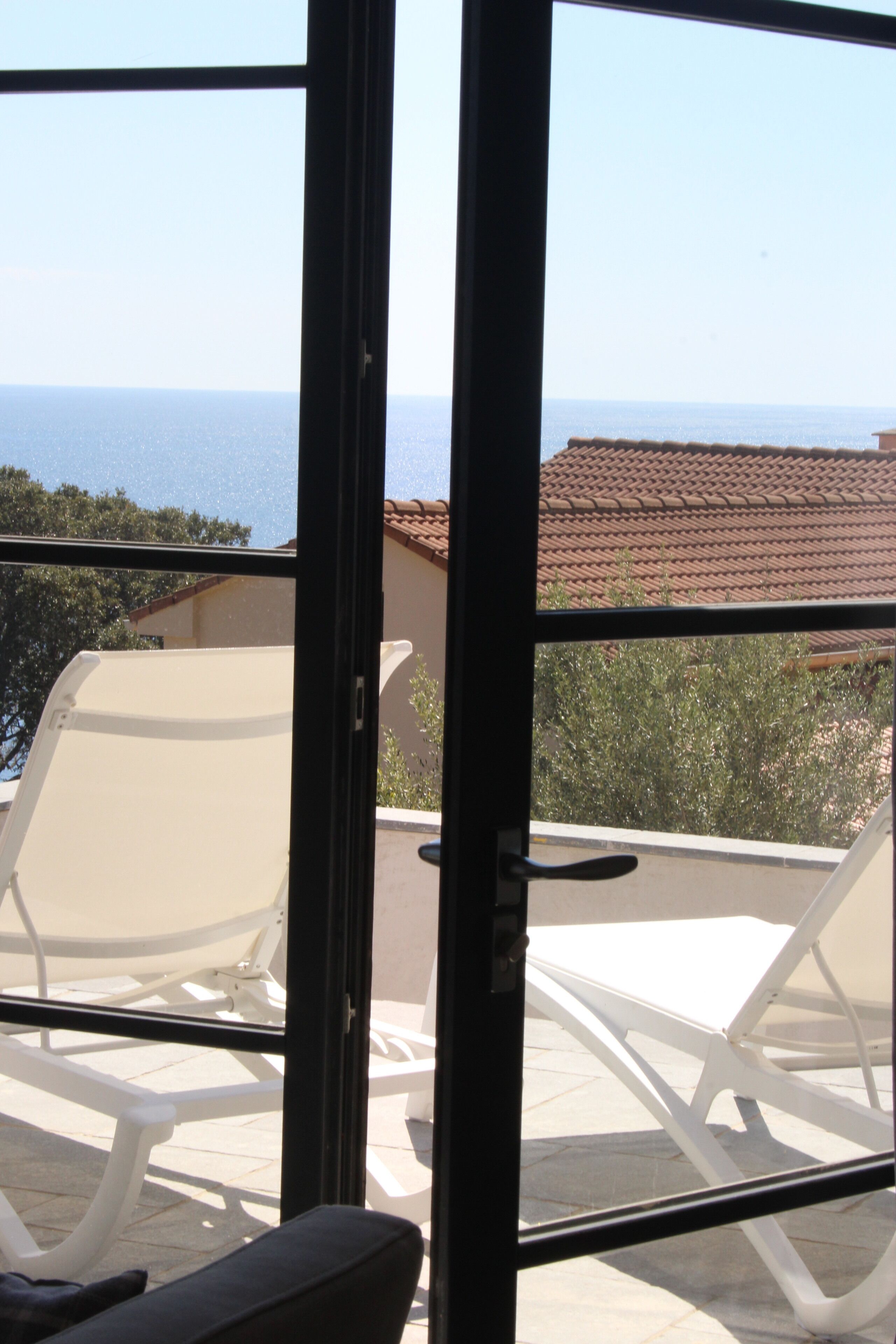 A balcony with white chairs and a view of the sea.