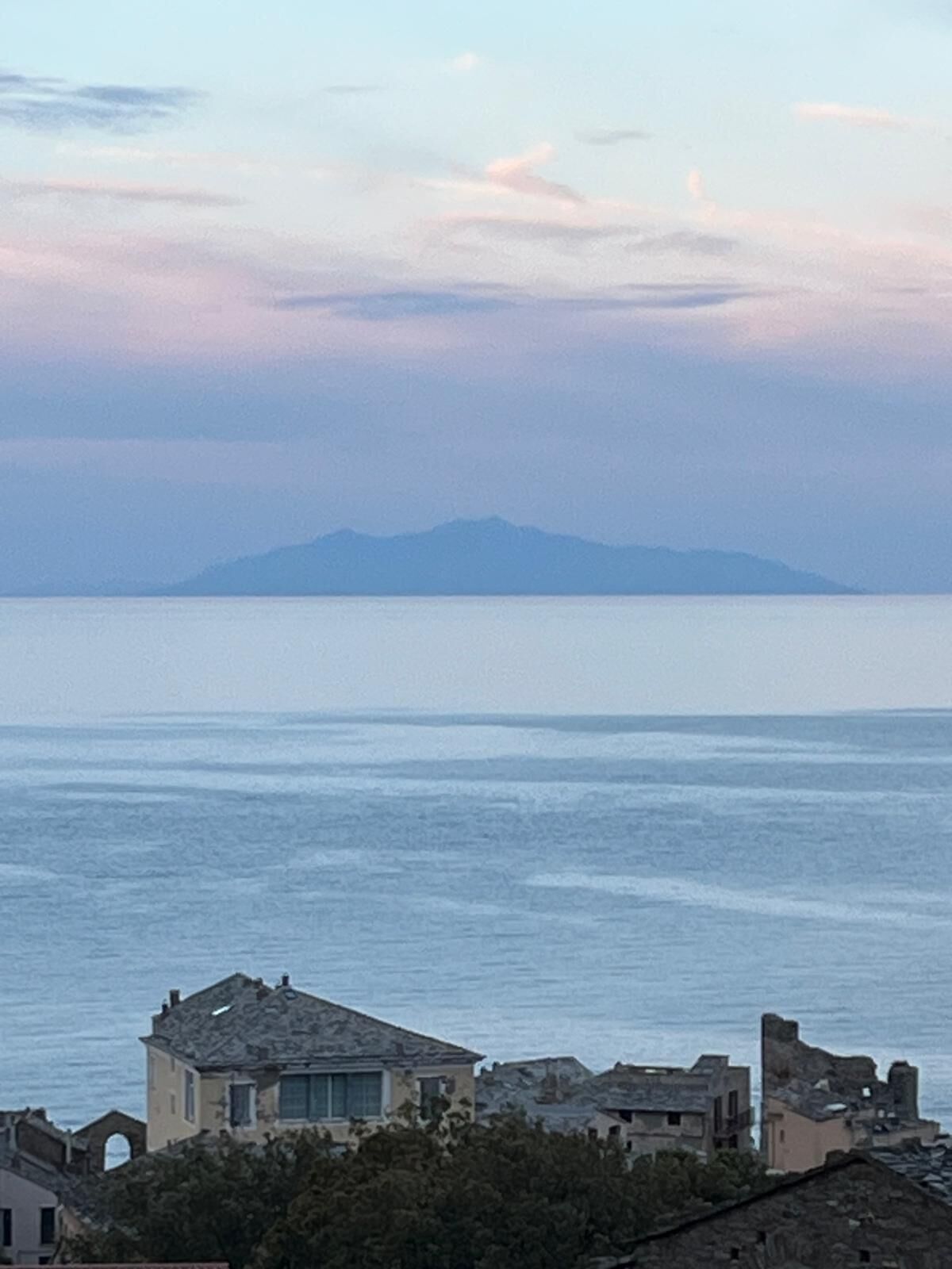 Une vue sur la côte, avec une montagne à l’horizon, des bâtiments au premier plan et un ciel dégagé.