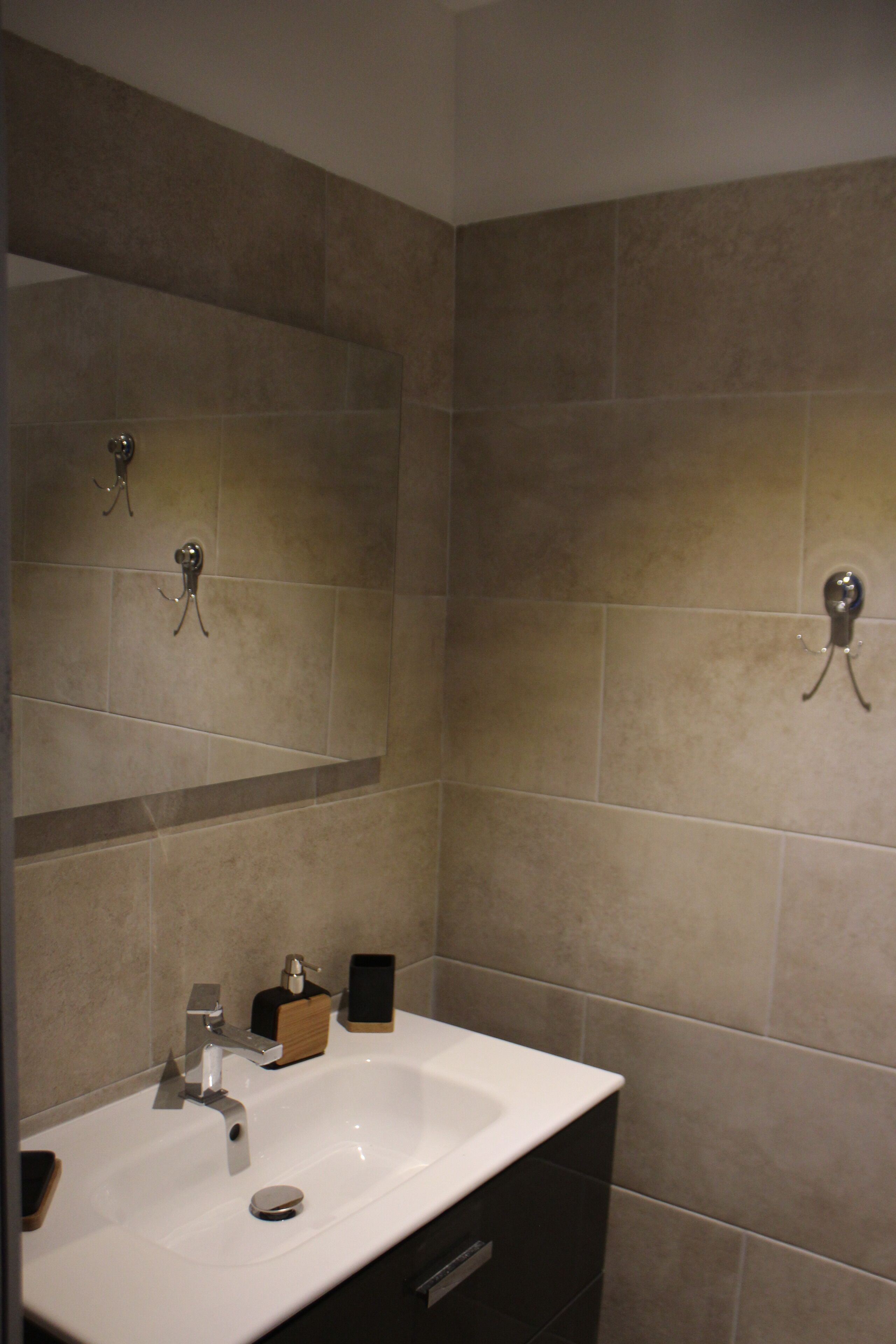 A bathroom with a white sink, a mirror, and beige tiles.