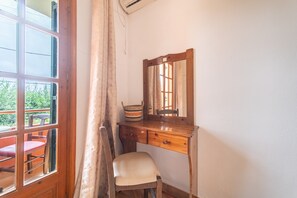 Une pièce avec un bureau en bois, une chaise, un miroir et une fenêtre avec des rideaux.
