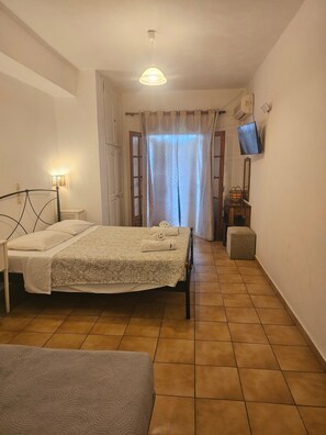 Un dormitorio con una cama, una mesita de noche, un televisor montado en la pared y una ventana con cortinas.