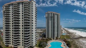 A high-rise hotel with multiple balconies, a swimming pool, and a beach view.