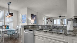 A kitchen with white cabinetry, granite countertops, a built-in dishwasher, and a dining area with a table and chairs.
