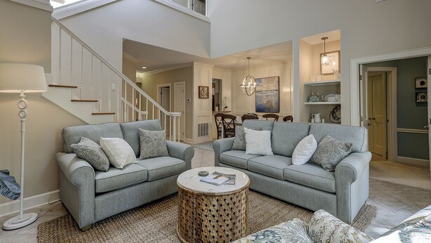 A spacious living room with two grey sofas, a round coffee table, and a staircase leading to an upper level.