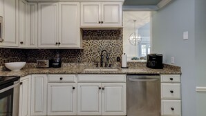 A kitchen with white cabinets, a tiled backsplash, a stainless steel dishwasher, and a coffee maker.