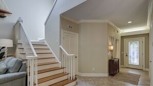 A spacious foyer with a wooden staircase, a grey sofa, and a rug on the floor.