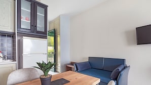 A compact living space with a kitchenette, a dining table with a plant, a blue sofa, and a flat-screen TV mounted on the wall. - Apartment in a Hotel 'Sunset Premium Studio 7' with Sea View, Shared Pool, & Wi-Fi (Lefkada)
