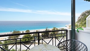 A balcony with a view of the sea and beach, a chair, and a table. - Apartment in a Hotel 'Sunset Premium Studio 7' with Sea View, Shared Pool, & Wi-Fi (Lefkada)