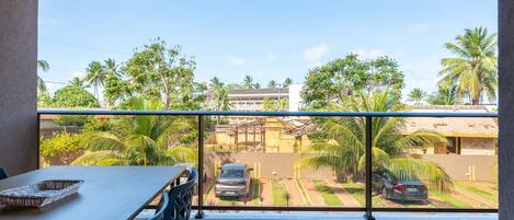 A balcony with a view of a street, palm trees, and parked cars.