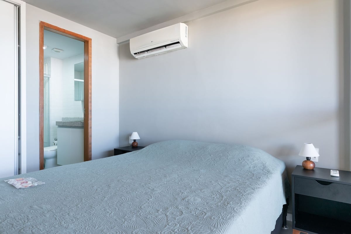 Ein Hotelzimmer mit Bett, Nachttischen, einer Klimaanlage und einem durchgegangenen Tür erkennbaren Badezimmer.