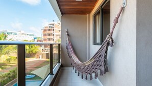 A balcony with a hammock, a pool, and a view of buildings and greenery. - Praia Central Porto de Galinhas (Ipojuca)