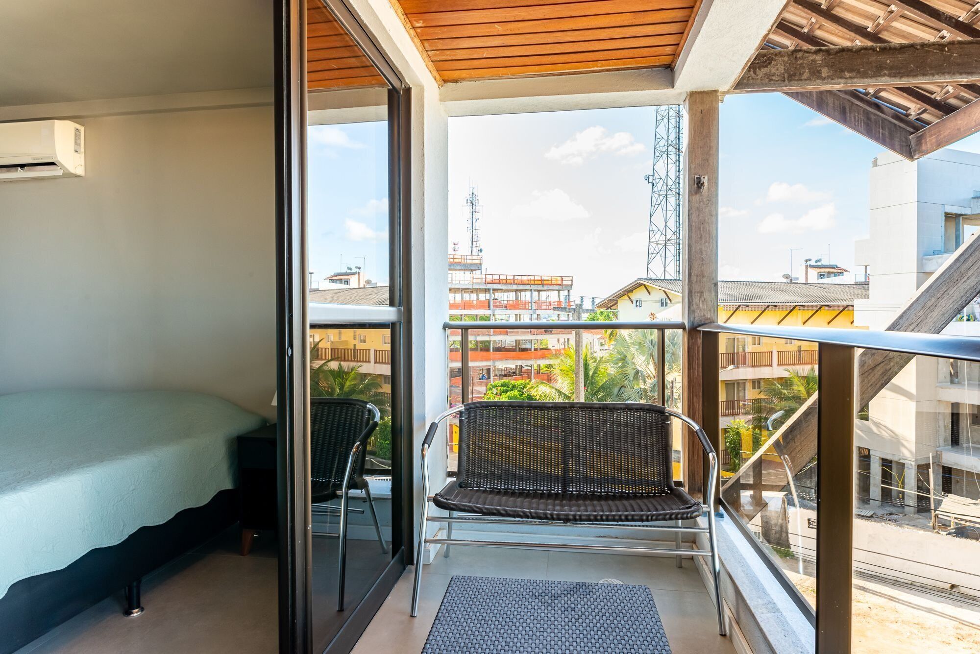 Ein Balkon mit einem Bett, einem Sessel und Blick auf Gebäude und einen Turm.