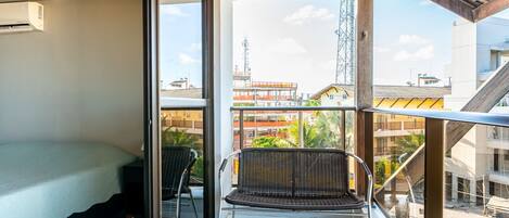 Ein Balkon mit einem Bett, einem Sessel und Blick auf Gebäude und einen Turm.
