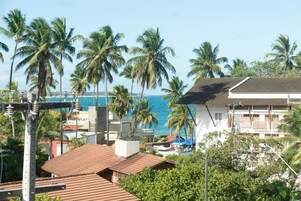 A coastal view with palm trees, a beach, and a white building with a tiled roof.