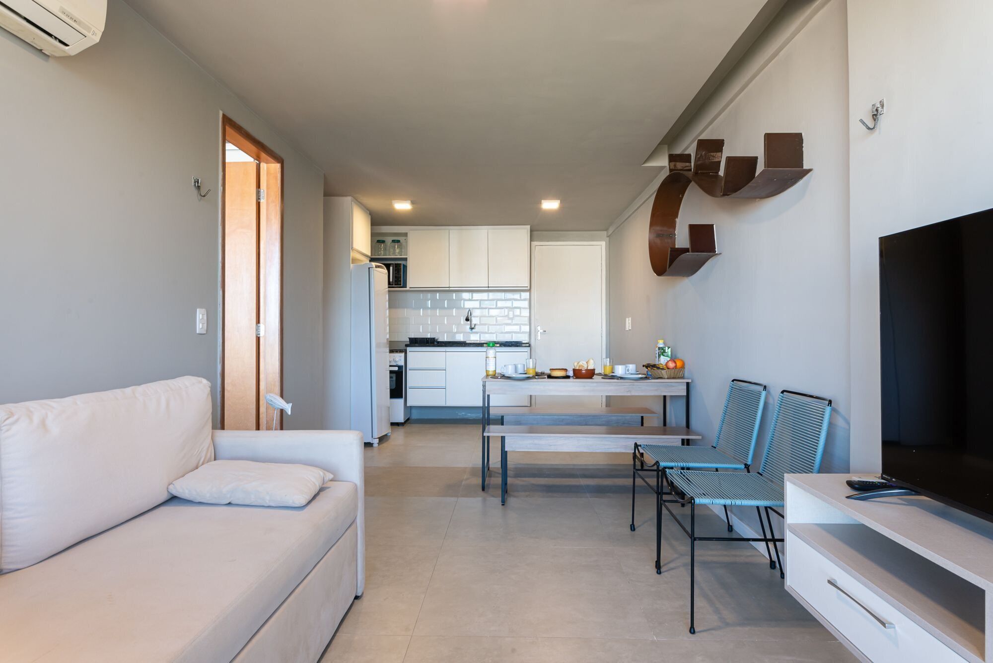 Una sala de estar moderna con un sofá, una mesa de comedor con sillas, una cocina al fondo y un televisor a la derecha.