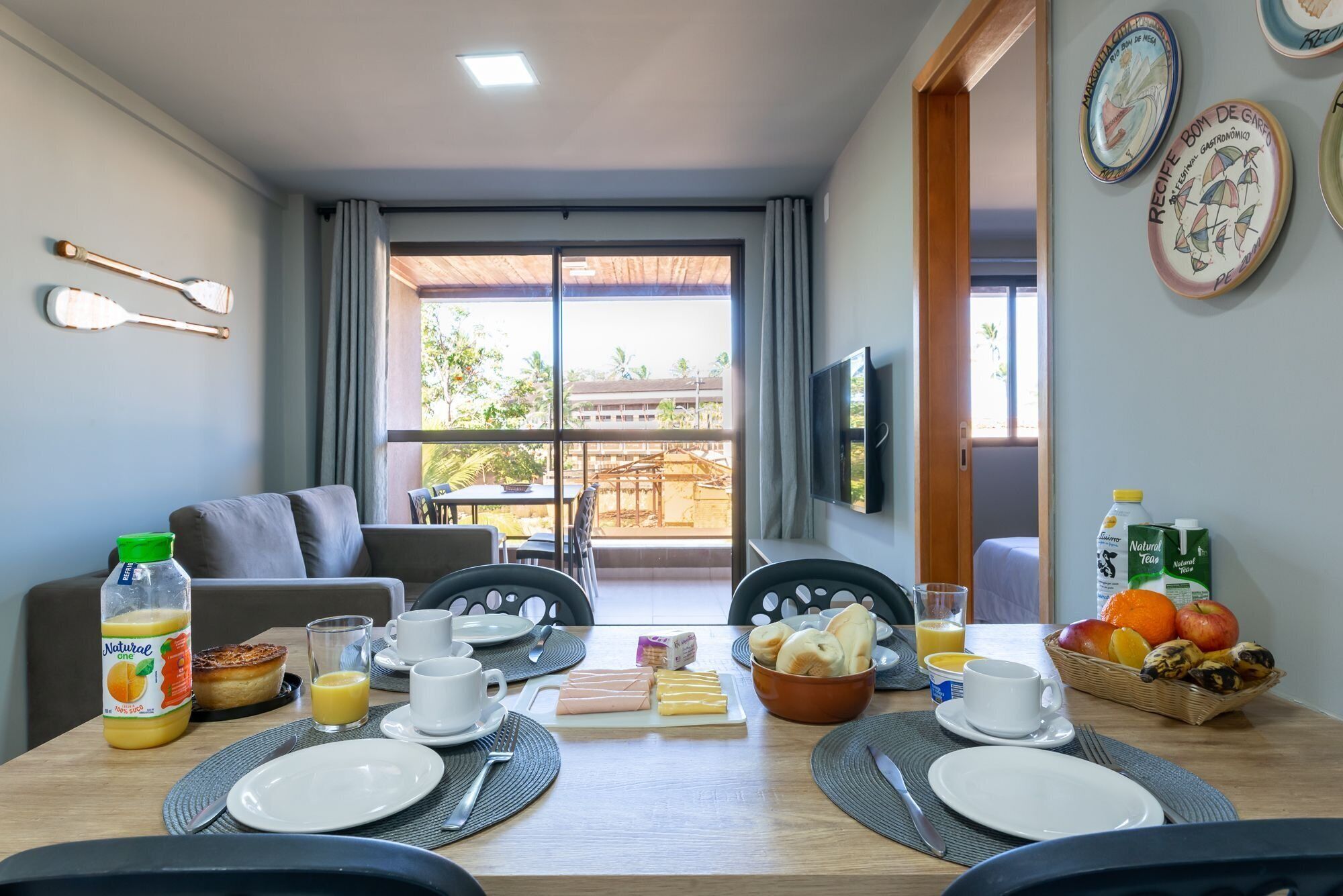 A dining area with a table set for breakfast, including plates, cups, and a bowl of fruit.