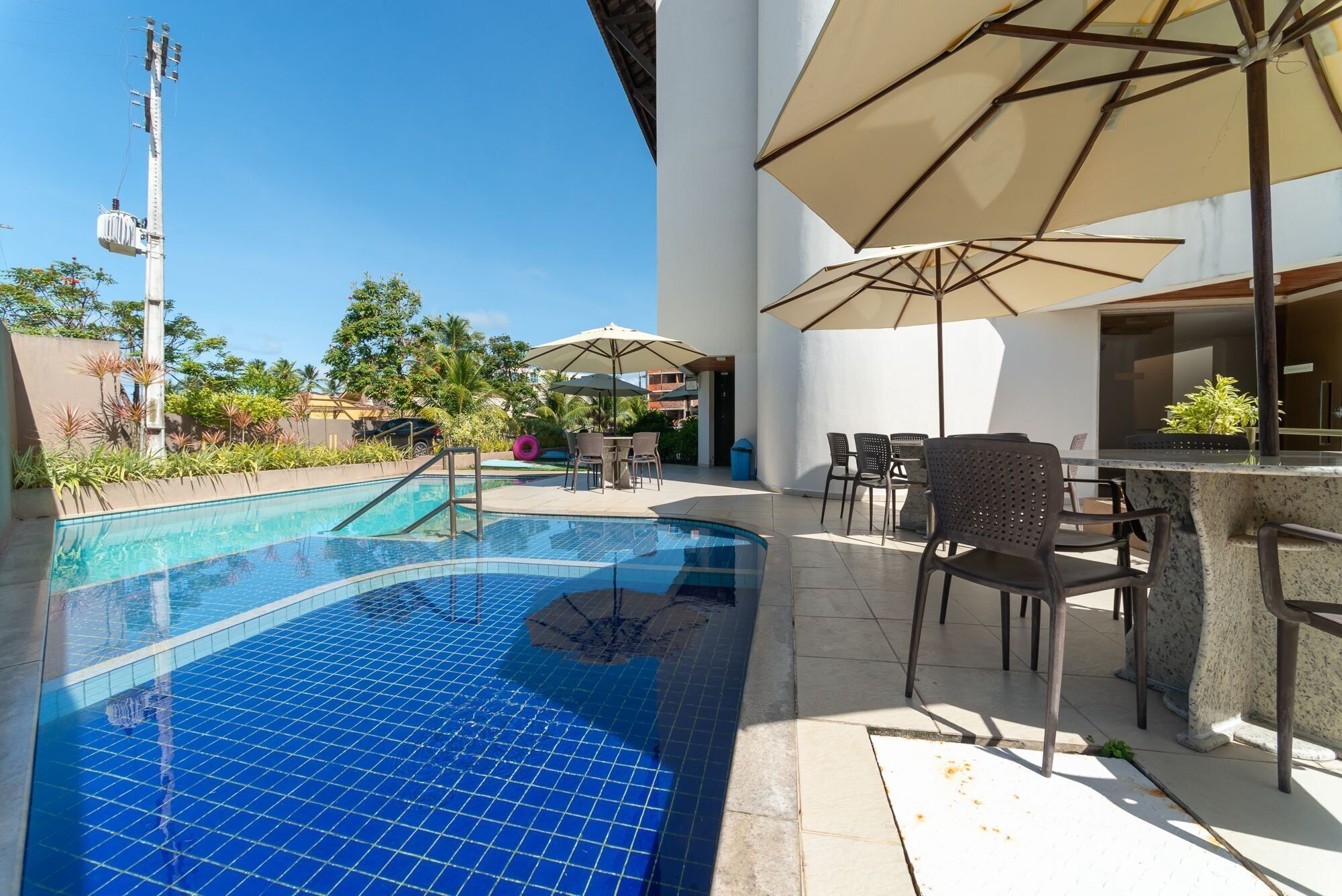 Une piscine avec une terrasse carrelée, des sièges extérieurs et des parasols.