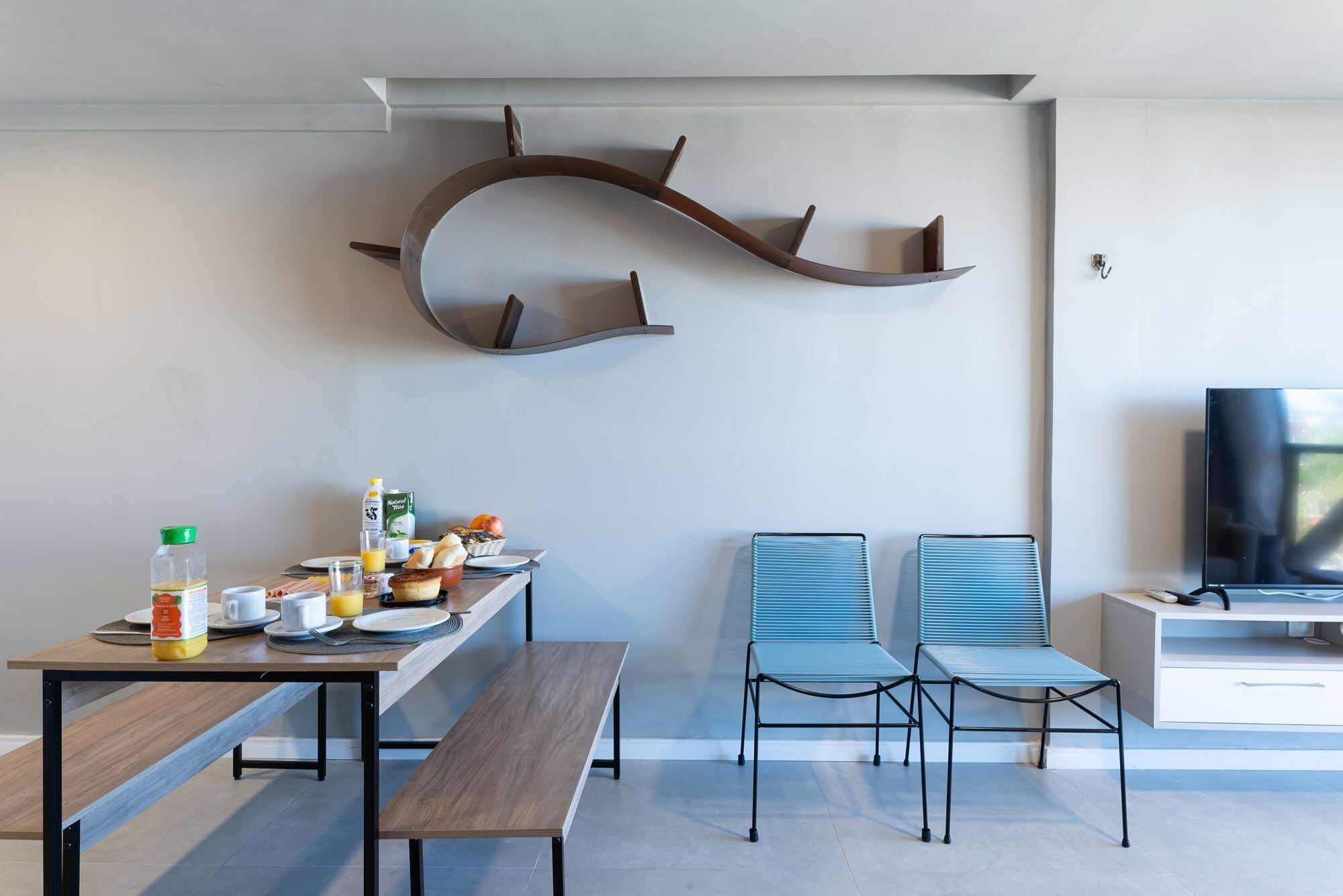 Un espace repas moderne avec une table en bois, des bancs et un téléviseur posé sur un meuble.