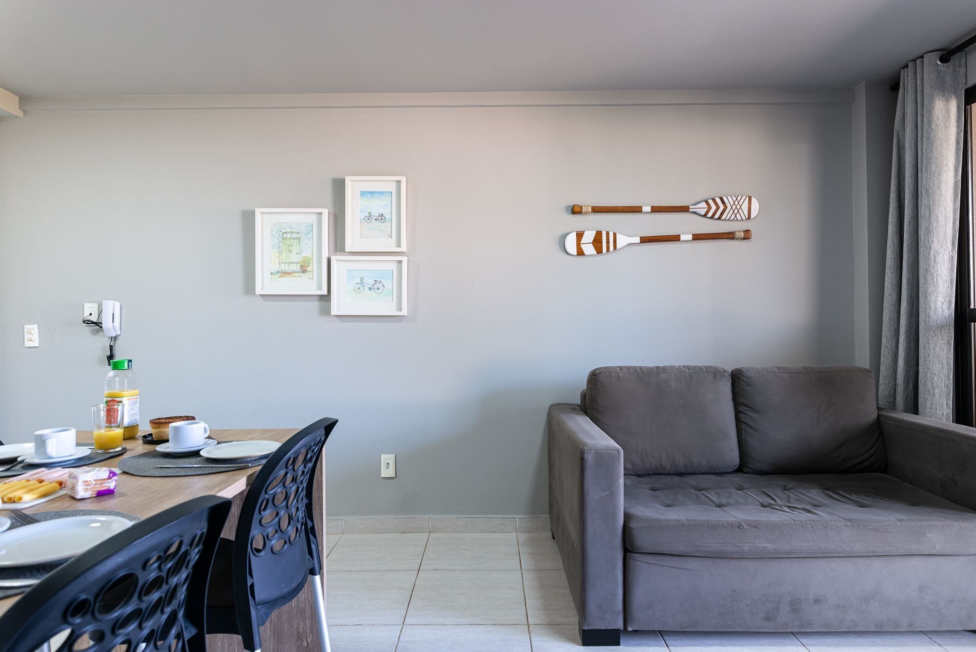 Un soggiorno moderno con un divano grigio, un'area pranzo con un tavolo apparecchiato per la colazione e due opere d'arte incorniciate al muro.