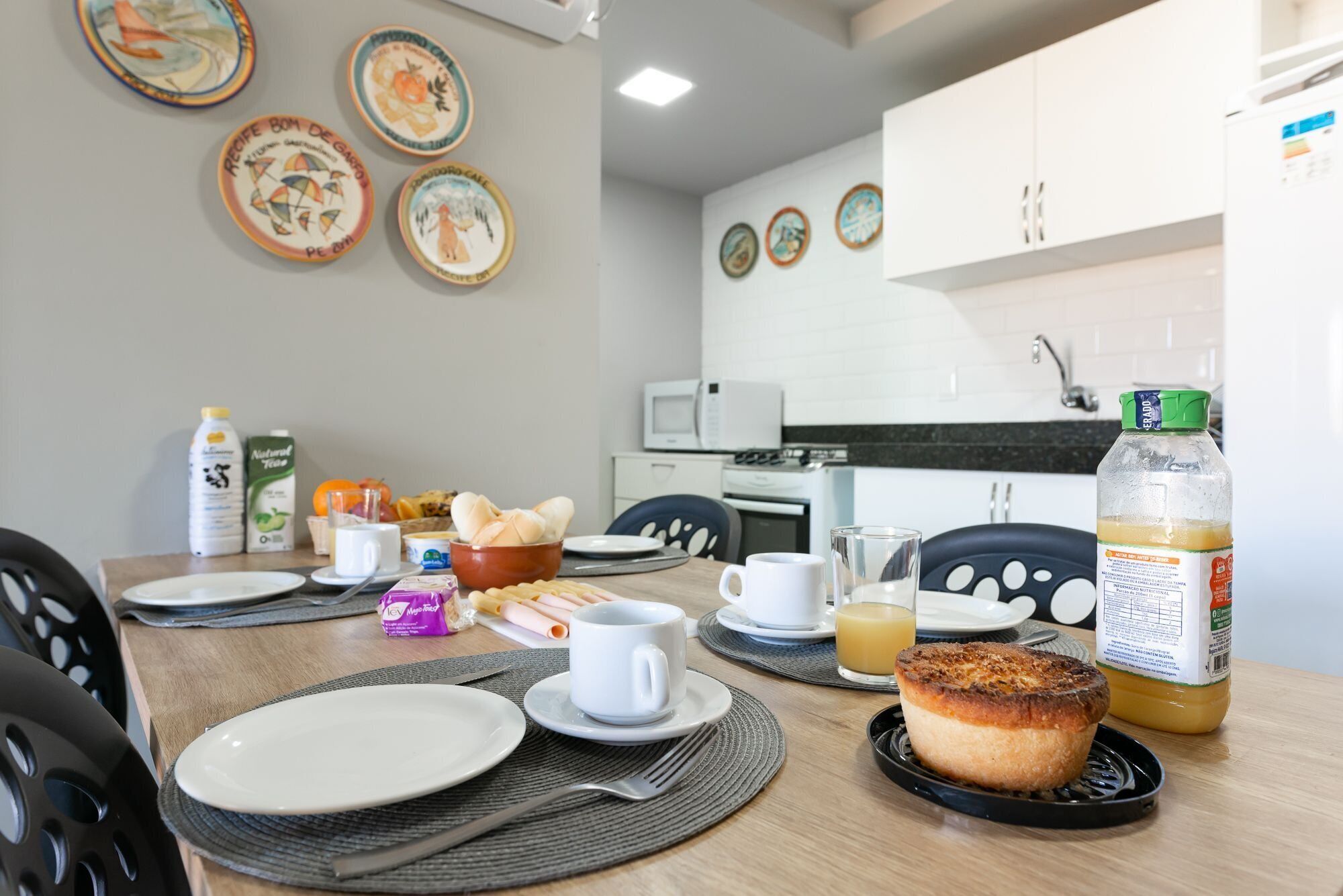 A breakfast table set with plates, cups, and food items in a modern kitchen with white cabinets and a microwave.