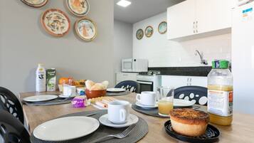 A breakfast table set with plates, cups, and food items in a modern kitchen with white cabinets and a microwave.