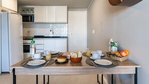 A modern kitchen with white cabinets, a microwave, and a stove. There is a dining table set with plates, cups, and a basket of fruit. - Praia Central Porto de Galinhas (Ipojuca)