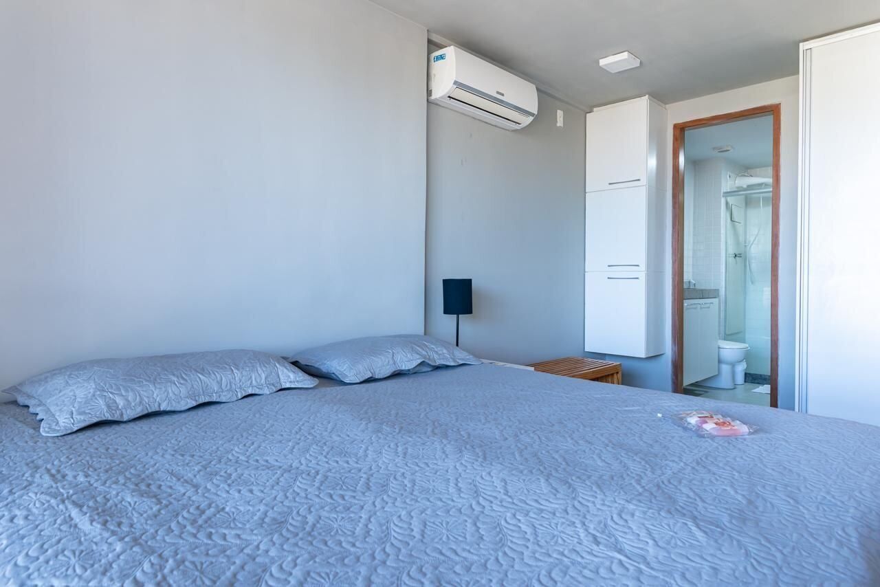 A bedroom with a bed, an air conditioning unit, a bedside table, and a mirror.
