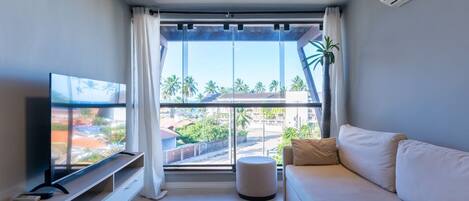 A modern living room with a large window, a flat-screen TV, a sofa, and a small ottoman.