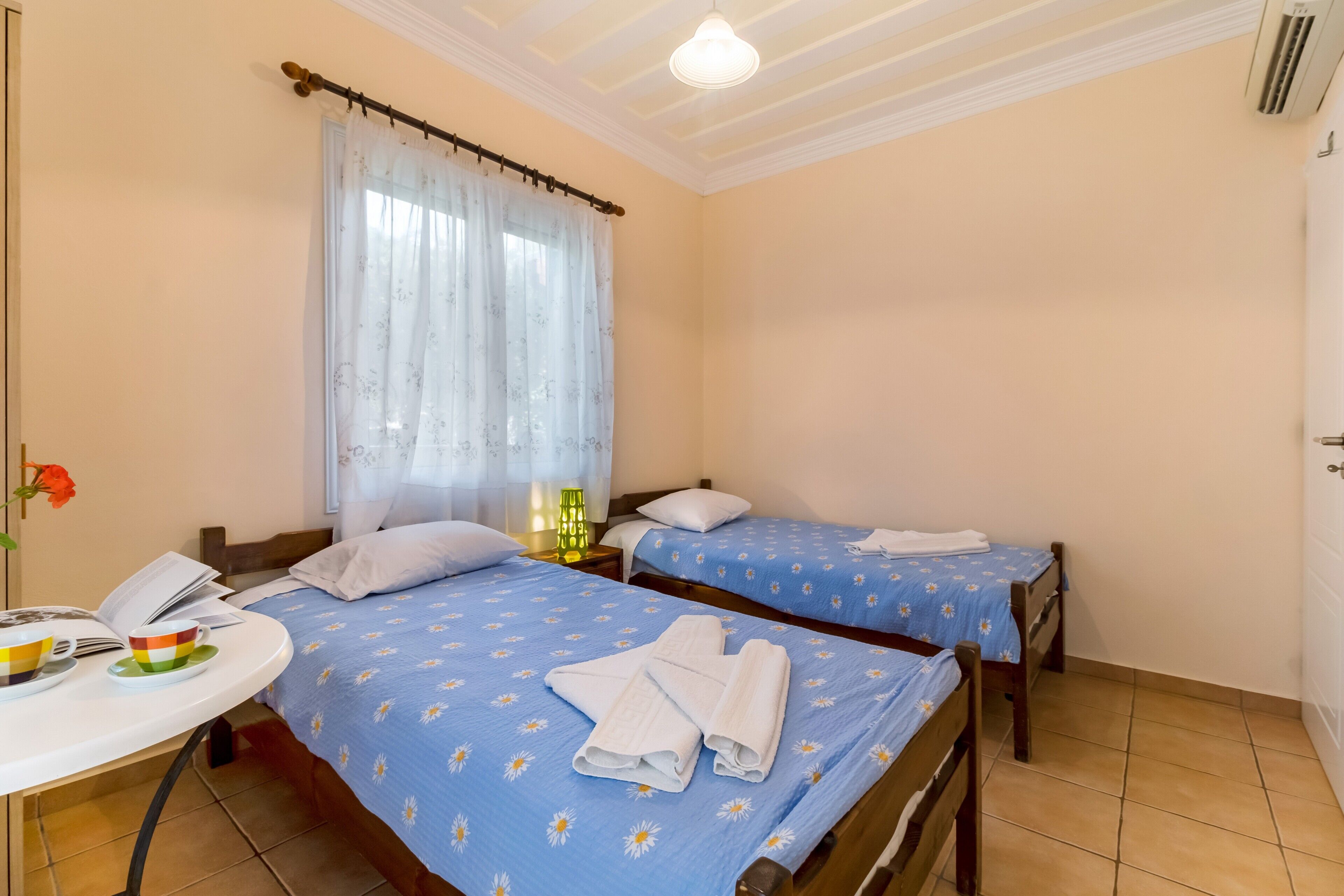 A hotel room with two beds, a small table with a phone and a cup, and a window with curtains.