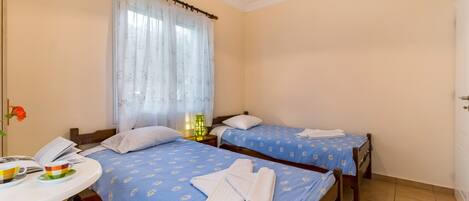 A hotel room with two beds, a small table with a phone and a cup, and a window with curtains.