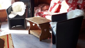 An attic room with a sloped ceiling, a wooden heater, a sofa, a chair, and a small table. - Chalets cocody norvégien (Jausiers)
