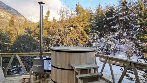 A wooden deck with a hot tub, wooden steps, and a view of snow-covered trees and mountains. - Chalets cocody norvégien (Jausiers)