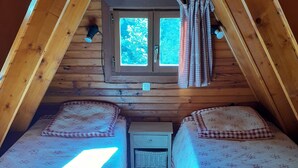 A small, cozy attic bedroom with two beds, a window with curtains, and a nightstand with a lamp. - Chalets cocody norvégien (Jausiers)