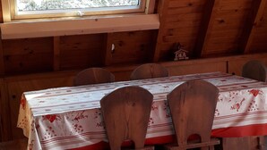 A wooden interior with a table and chairs, a window with a view of snow-covered trees, and a fur throw on a chair. - Chalets cocody norvégien (Jausiers)