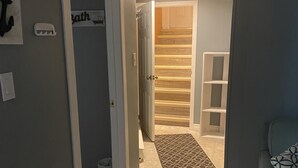 Un couloir avec un sol carrelé, une porte donnant sur une pièce et une chaise bleue.