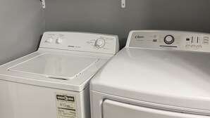 Un espace buanderie comprenant deux machines à laver à chargement frontal, une étagère avec des serviettes pliées et une bouteille de lessive.