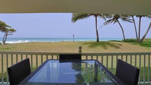 Ein Tisch mit Glasplatte und Korbstühle auf einem Balkon mit Blick auf einen Strand mit Palmen.