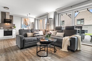 Een moderne woonkamer met een hoekbank, een ronde salontafel en een groot raam met uitzicht op het omliggende landschap.