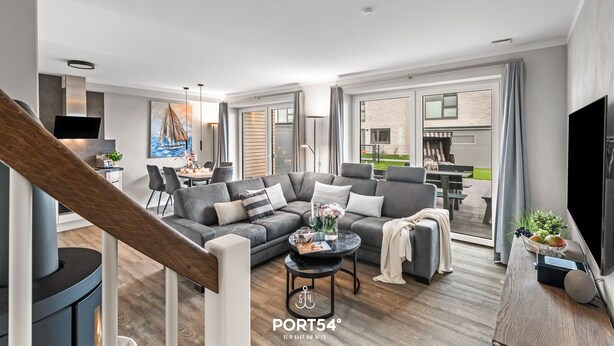 A modern living room with a grey sectional sofa, a coffee table, and a TV. There is a staircase with a wooden handrail leading to an upper floor. - Momme II - close to the North Sea and the beach, sauna, terrace, modern (Büsum)